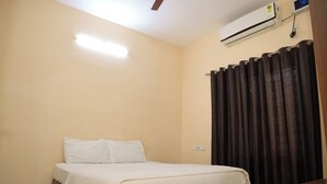 A bedroom with a bed, a ceiling fan, an air conditioning unit, and a window with dark curtains. - AK Vellore Stays  (Vellore)