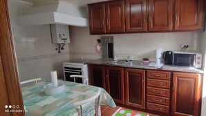 A compact kitchen with wooden cabinets, a microwave, a kettle, and a small dining area with a table and chairs. - Pretty town house located next to the medieval town of Penela and its castle.  (Penela)