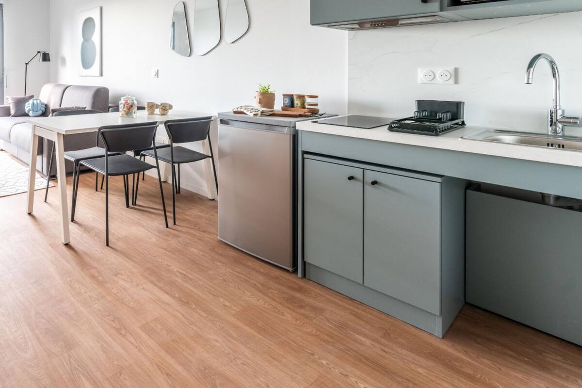 A modern kitchen with a dining area, a built-in dishwasher, and a large window offering a city view.