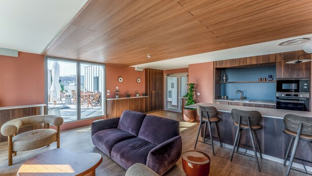 A modern living area with a sofa, chairs, a coffee table, a bar area with stools, and a kitchen with a microwave and sink.