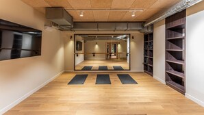 A spacious room with a wooden floor, a large mirror, and a yoga mat aligned in the center.