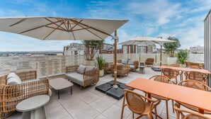 A rooftop patio with wicker furniture, outdoor tables, and umbrellas.