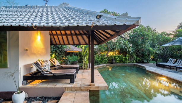 A poolside area with lounge chairs, a pergola, and a clear pool.