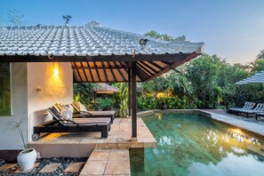Zona junto a la piscina con sillones de descanso, una pérgola y una piscina cristalina.