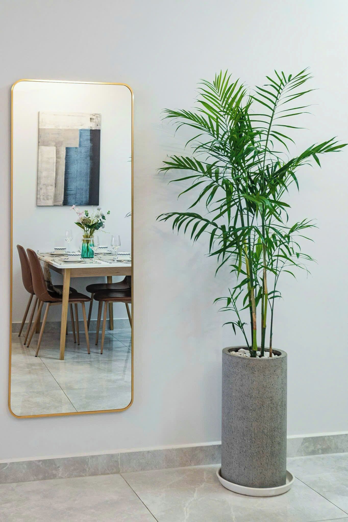 A dining area with a table set for four, a tall potted plant, and a large mirror on the wall.