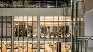A multi-level commercial space with glass walls, featuring a gym on the lower level and a seating area with yellow chairs on the upper level. - Luxury Apartment in Phu My Hung (Ho Chi Minh City)