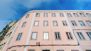 Un edificio de varios pisos con fachada rosa, múltiples ventanas y cables eléctricos visibles.