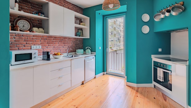 Una cocina moderna con gabinetes blancos, pared de ladrillo, paredes color aguamarina y suelo de madera.