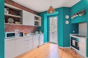 A modern kitchen with white cabinets, a brick wall, teal walls, and a wooden floor. - Monica's Place, a Friends Inspired Flat (Lisbon)