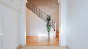 Una escalera con detalles de madera, paredes blancas y una planta en maceta al pie.