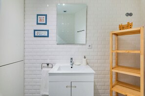 A bathroom with a white sink, mirror, and a wooden shelf.
