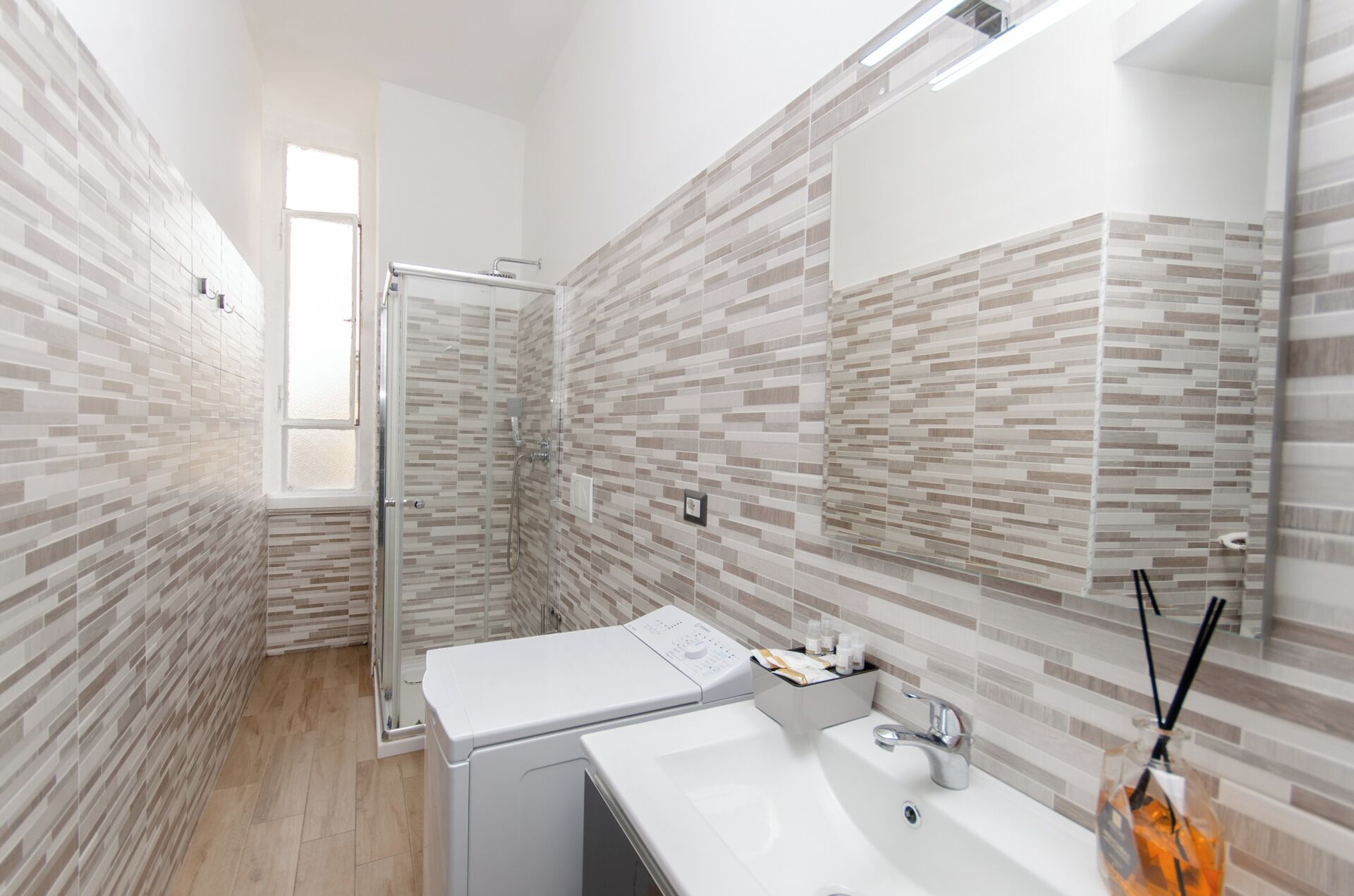 Un baño moderno con cabina de ducha de vidrio, lavadora integrada y tocador con espejo y lavamanos.