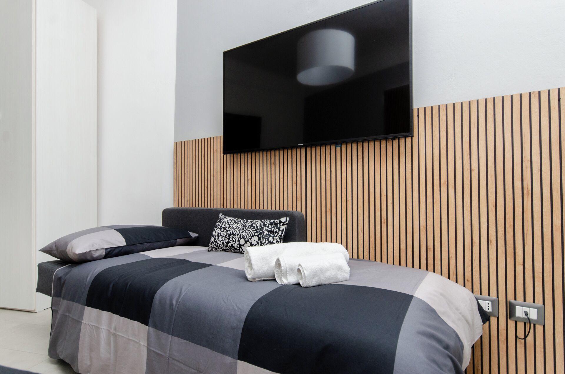 Une chambre à coucher moderne avec un lit, un téléviseur fixé au mur et un décor mural en panneaux de bois.