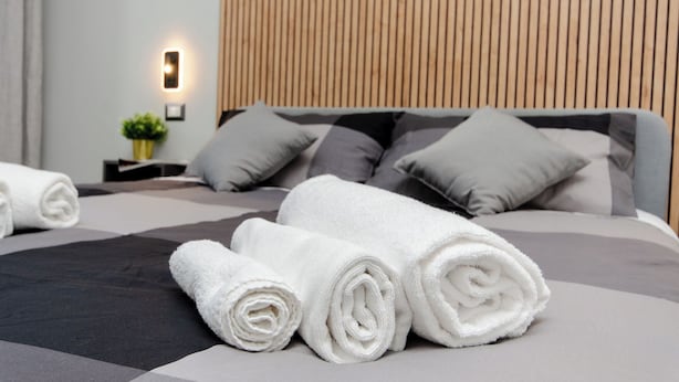 Ein ordentlich gemachtes Bett mit aufgerollten weißen Handtüchern, einer grau-schwarzen Bettdecke und grauen Kissen.