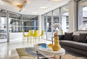 Um interior moderno com parede de vidro, um sofá, cadeiras amarelas e uma mesa de centro.