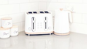 Una cocina con un tostador blanco, un hervidor y tres frascos de especias etiquetados como 'Té', 'Azúcar' y 'Café'.