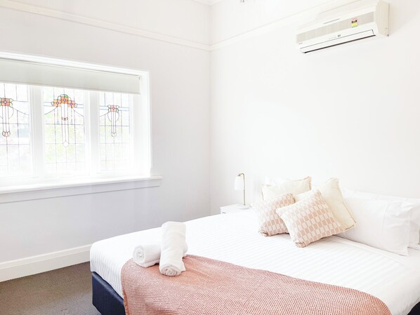 A hotel room with a bed, a window with stained glass, and an air conditioning unit.