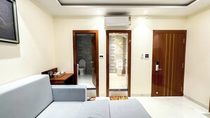 Una habitación de hotel moderna con sofá, una mesita con una bandeja de objetos, un baño con inodoro y lavabo, y una puerta de madera.