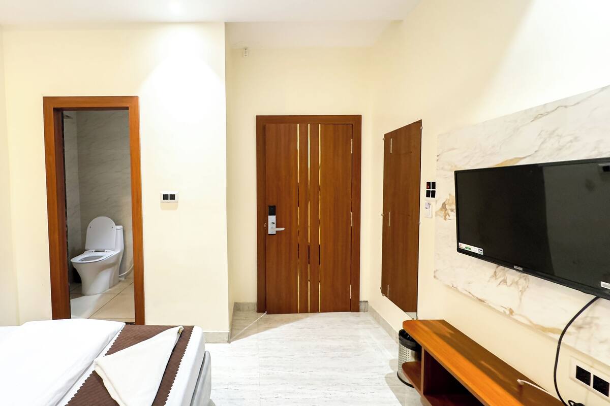 A hotel room with a bed, a TV, a wooden wardrobe, and a bathroom with a toilet.