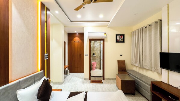 A modern hotel room with a bed, a TV, a seating area, and a bathroom with a shower and toilet. - Hotel Vibes of Kashi (Varanasi)