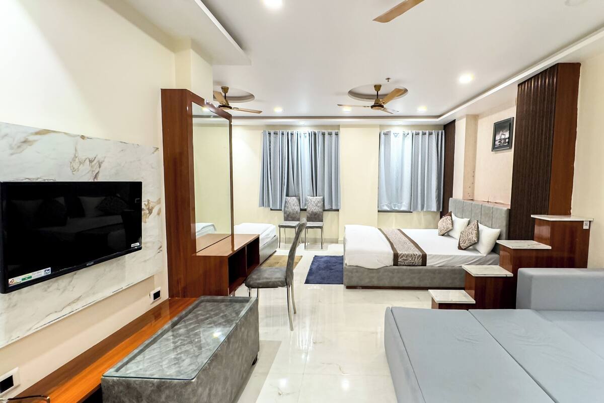 A modern hotel room with a flat-screen TV, a sofa, a bed, a desk, and a ceiling fan.