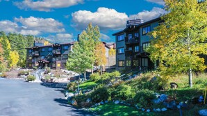 Un immeuble à plusieurs étages doté de balcons, d’un chemin pavé de pierres et entouré de verdure.