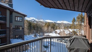 Un balcon avec vue sur des montagnes enneigées, un barbecue abrité et un mur en pierre.