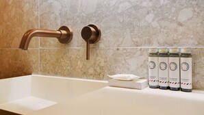 A bathroom with a white sink, a copper faucet, and a set of shower gel bottles on the counter.