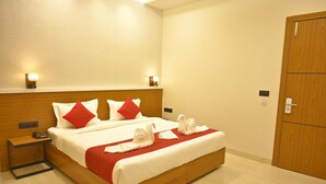 A hotel room with a wooden bed, red and white pillows, two bedside lamps, a wooden nightstand, and a wooden door. - Hotel 7b (Chhatarpur)