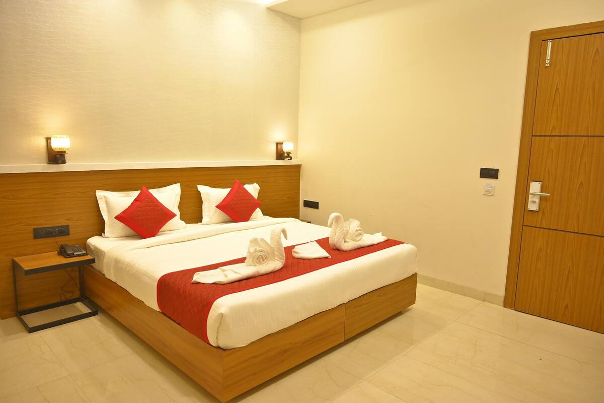 Quarto de hotel com cama de madeira, almofadas vermelhas e brancas, duas luminárias de cabeceira, mesa de cabeceira de madeira e porta de madeira.