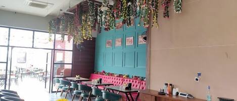 Een restaurant met een blauwe muur, roze zachte zitplaatsen en hangende planten.
