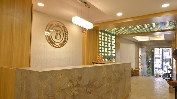 A reception area with a marble reception desk, a logo on the wall, and a decorative wall panel. - Hotel 7b (Chhatarpur)
