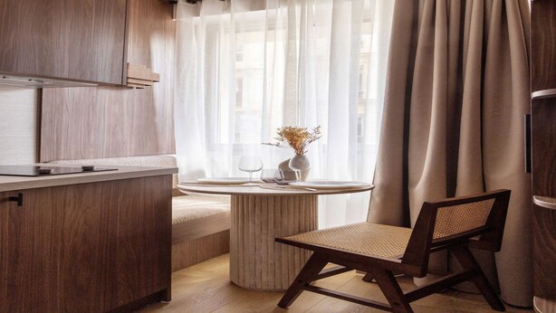 Una cocina moderna con armarios de madera, una mesa redonda con una silla y una ventana con cortinas de gasa.