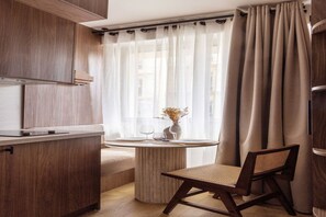 A modern kitchen with wooden cabinets, a round dining table with a chair, and a window with sheer curtains. - Magnificent Studio with A/C - 1P - Champs-Élysées (Paris)