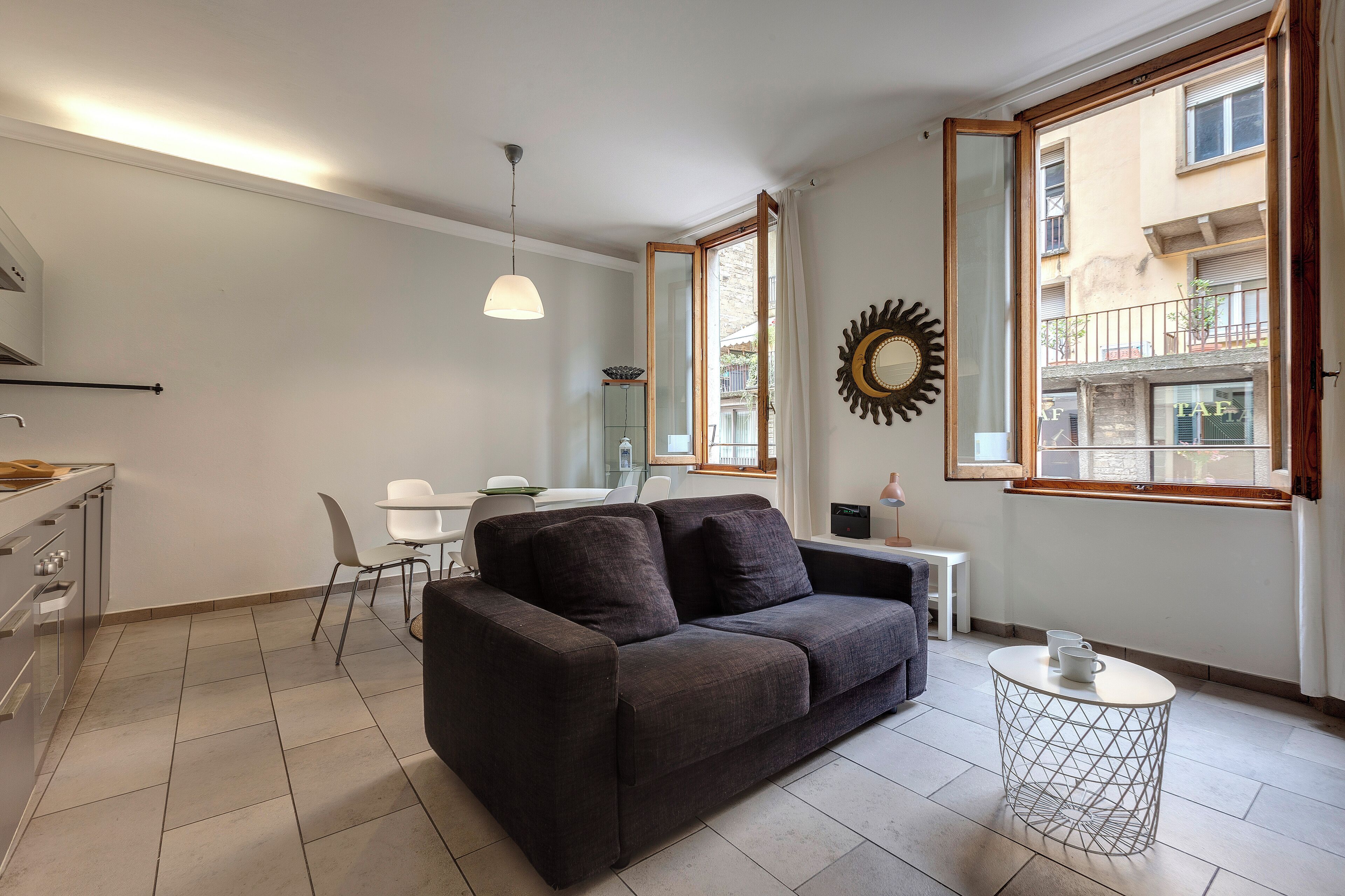 A modern living room with a dark sofa, a small round table, and a dining area with a white table and chairs.