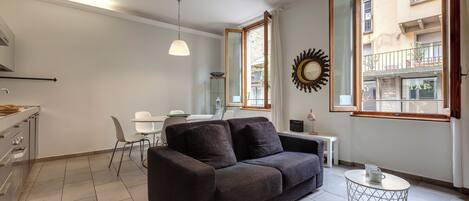 Una sala moderna con un sofá oscuro, una mesita redonda y un comedor con una mesa y sillas blancas.