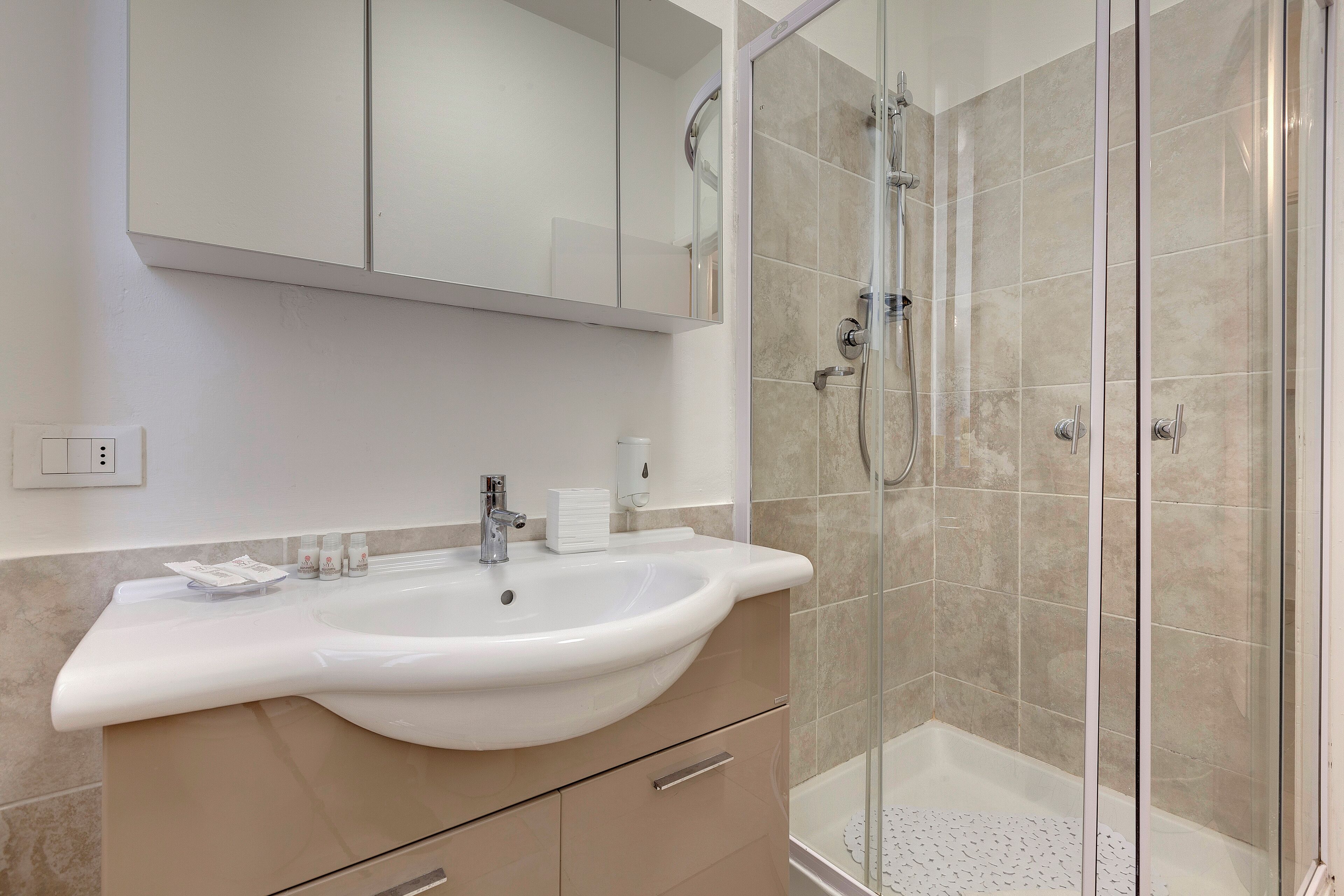 A bathroom with a white sink, beige tiles, a glass shower enclosure, and a mirror above the sink.