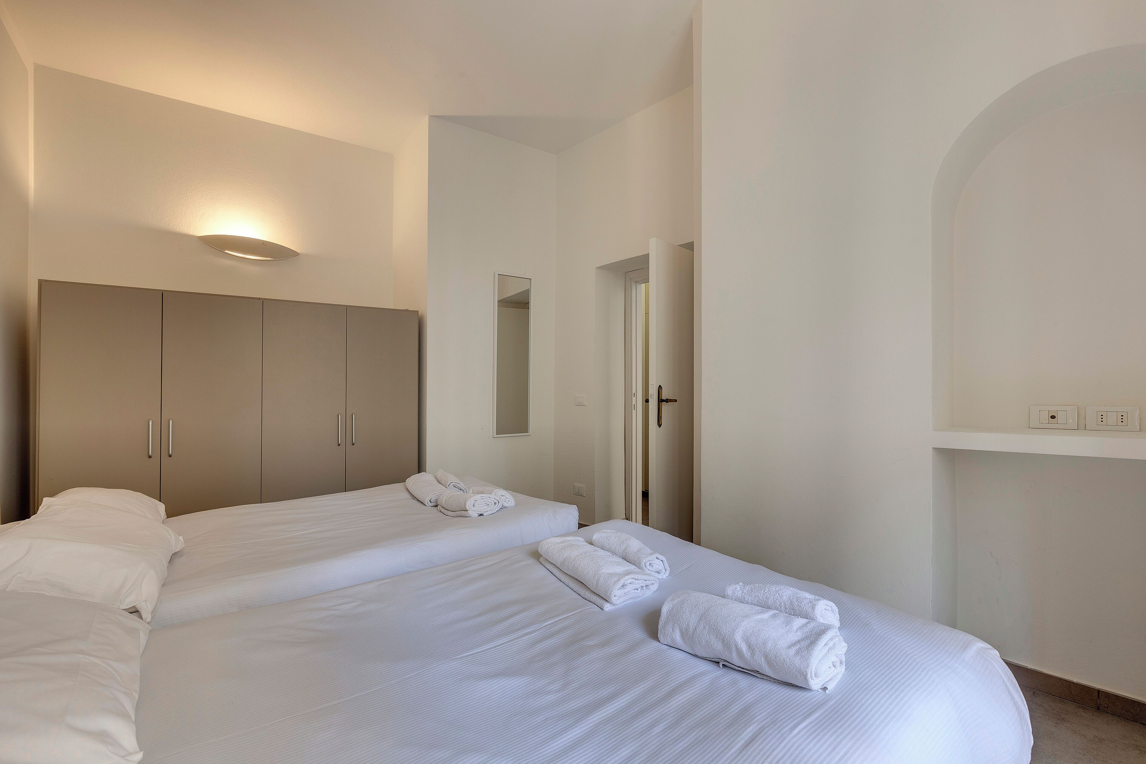 Una habitación de hotel con dos camas, un armario, un espejo y una puerta.