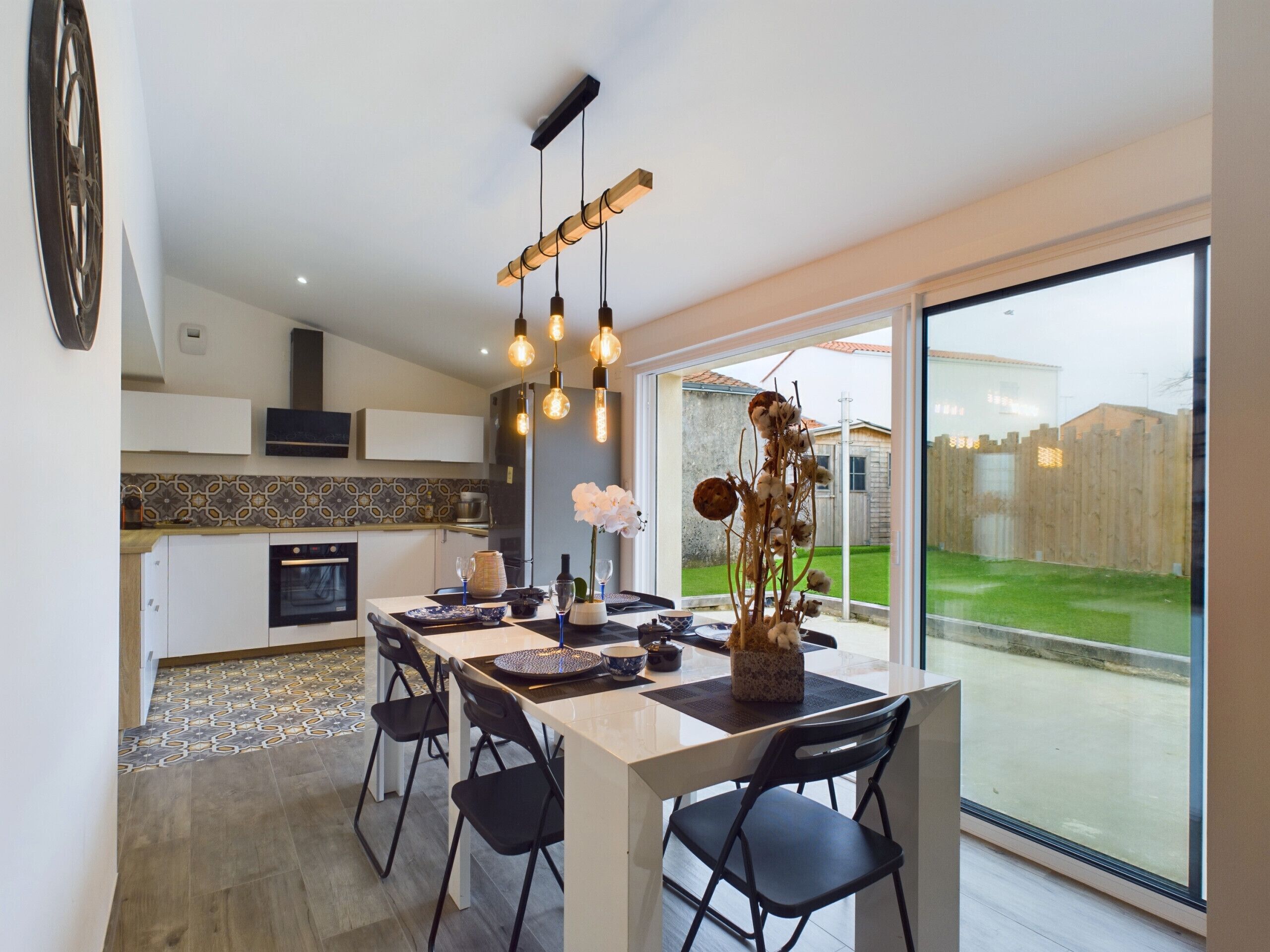 Eine moderne Küche mit Essbereich, ausgestattet mit einem großen Fenster, Pendelleuchten und Blick auf den Garten.