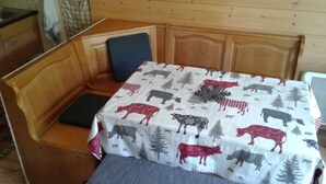 A small, cozy room with a wooden headboard and bench seating. A table with a cow and tree pattern tablecloth is placed in the center. - Studio 4 persons Châtel / Linga. Chairlift within walking distance. (Châtel)