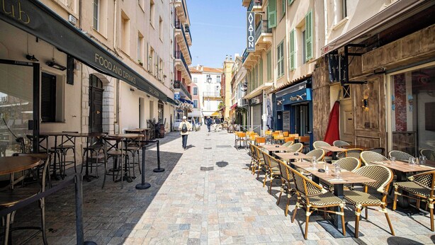 A narrow street with outdoor seating and a variety of shops and cafes.