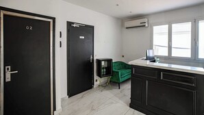 A room with two black doors, one marked with the number 02, a green sofa, a marble-tiled floor, and a window with blinds.