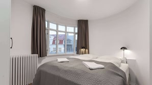 Ein modernes Hotelzimmer mit einem großen Bett, einem Fenster mit Vorhängen, einem Heizkörper und einer Lampe.