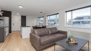 Eine moderne Wohnung mit Küchenzeile, Essbereich, Wohnzimmer mit Sofa und großen Fenstern mit Stadtblick.
