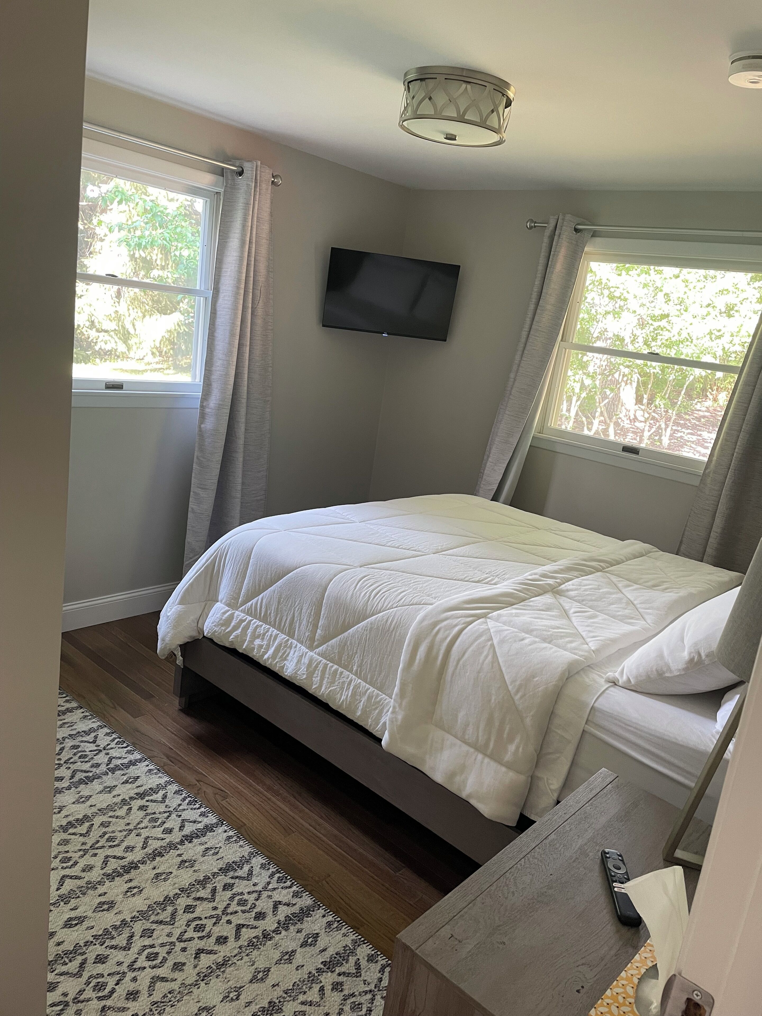 Un dormitorio con cama, televisor montado en la pared y ventana con cortinas.