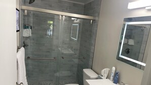 Een moderne badkamer met een douchecabine van glas, een wit toilet en een wastafelmeubel met een wastafel en spiegel.