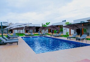 A swimming pool with lounge chairs and umbrellas, surrounded by modern buildings.