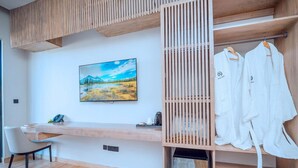 A modern room with a wooden desk, a painting of a landscape, and a clothing rack with white robes. - Solai Oasis (Namanga)
