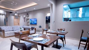 A modern dining area with wooden tables and chairs, a sofa, and a TV mounted on the wall. - Solai Oasis (Namanga)
