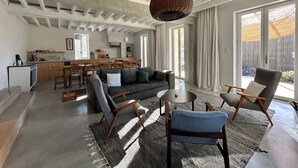 Ein großzügiger Wohnbereich mit einer Couch, Sesseln, einem Couchtisch und einer Küche im Hintergrund.